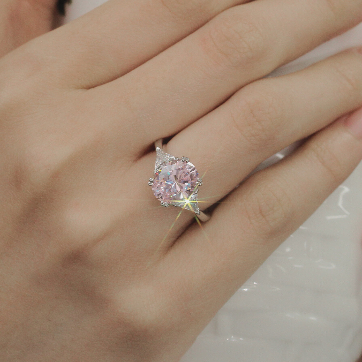 Close-up of a hand wearing a ring with a pink gemstone on a neutral background