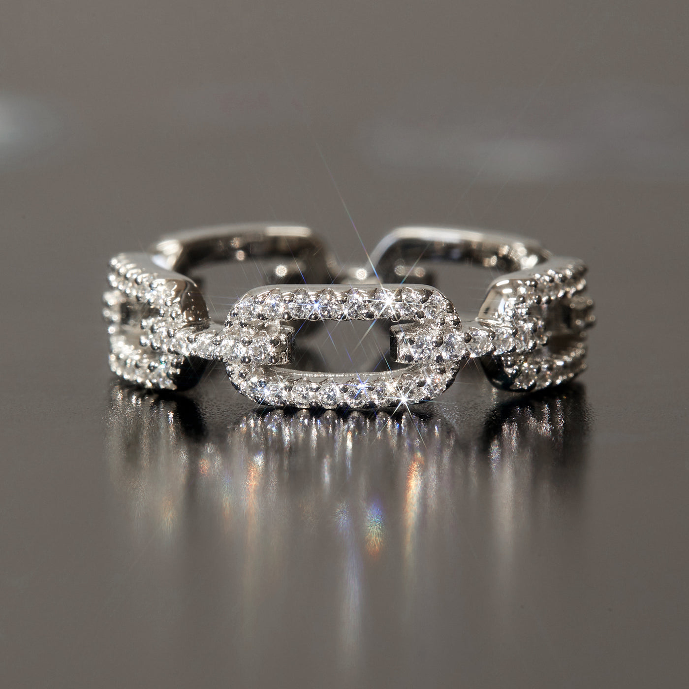 Silver chain-link ring with diamonds on a reflective surface