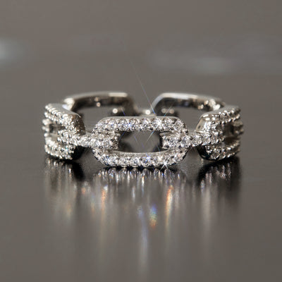 Silver chain-link ring with diamonds on a reflective surface