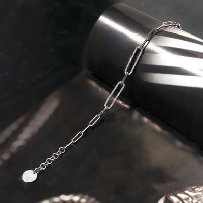Silver chain bracelet on a dark surface with a cylindrical object