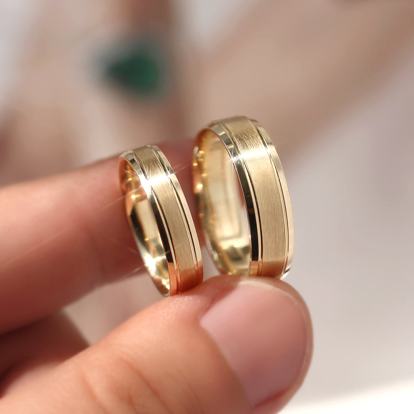 Two gold rings held between fingers against a blurred background