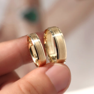 Two gold rings held between fingers against a blurred background