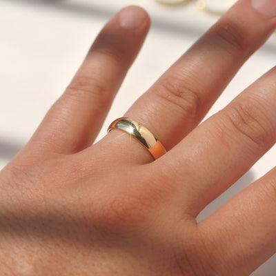 Close-up of a hand wearing a gold ring on a neutral background
