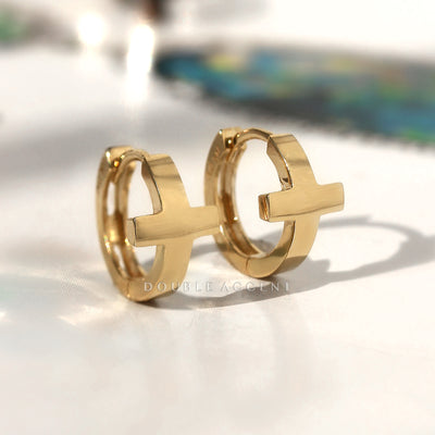 Solid 14K gold cross huggie hoops on white background