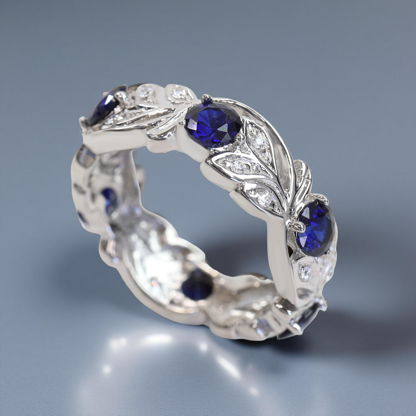 Silver ring with blue gemstones and leaf designs on a gray background