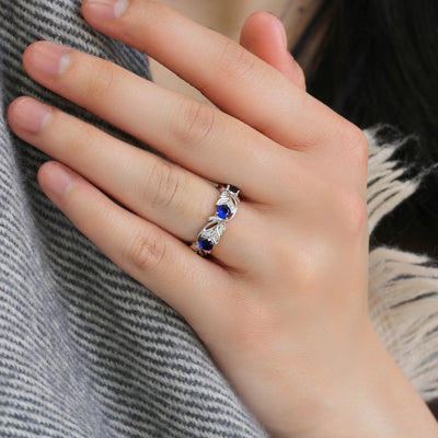 Hand wearing a silver ring with blue gemstones on a textured fabric background
