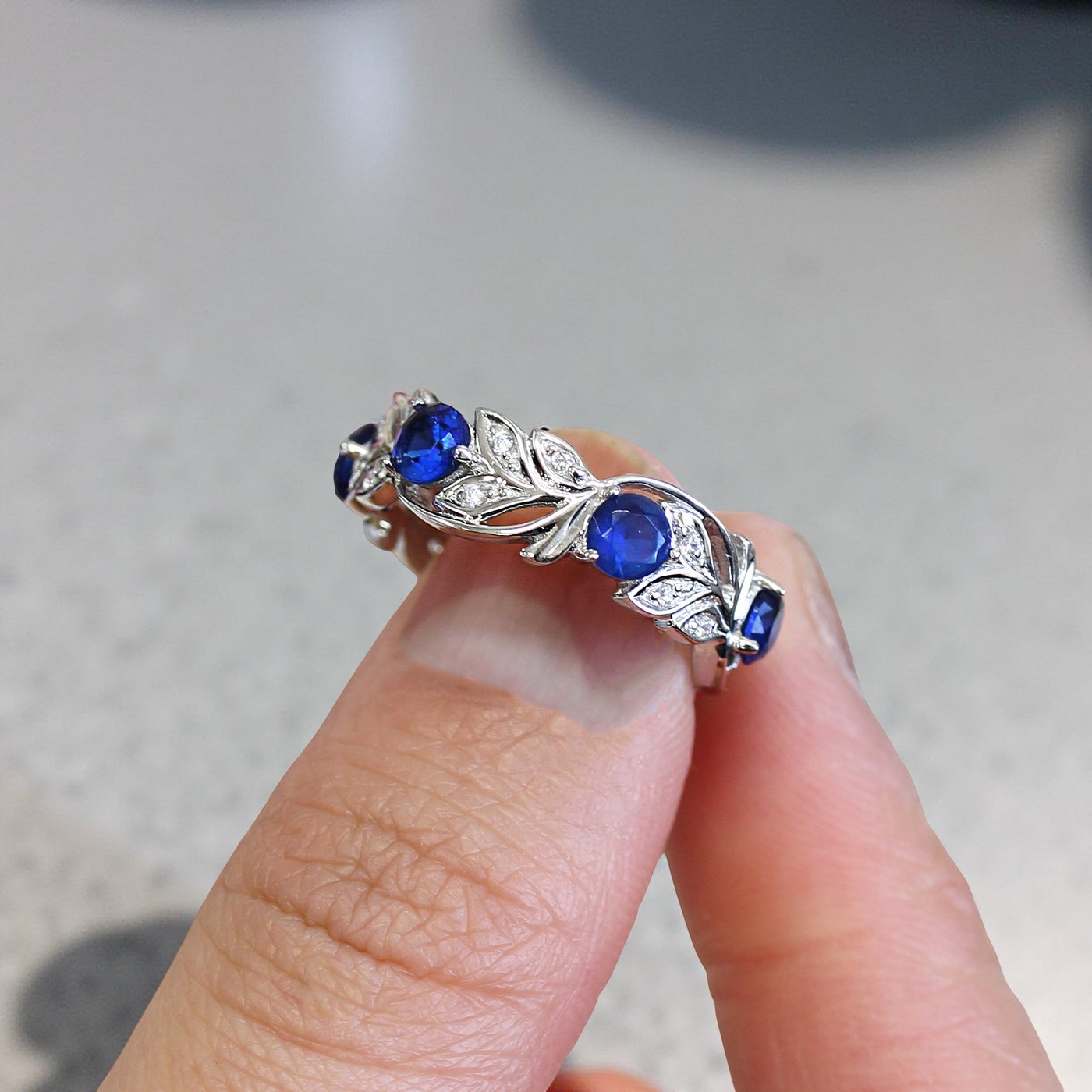 Silver ring with blue gemstones held between fingers against a neutral background