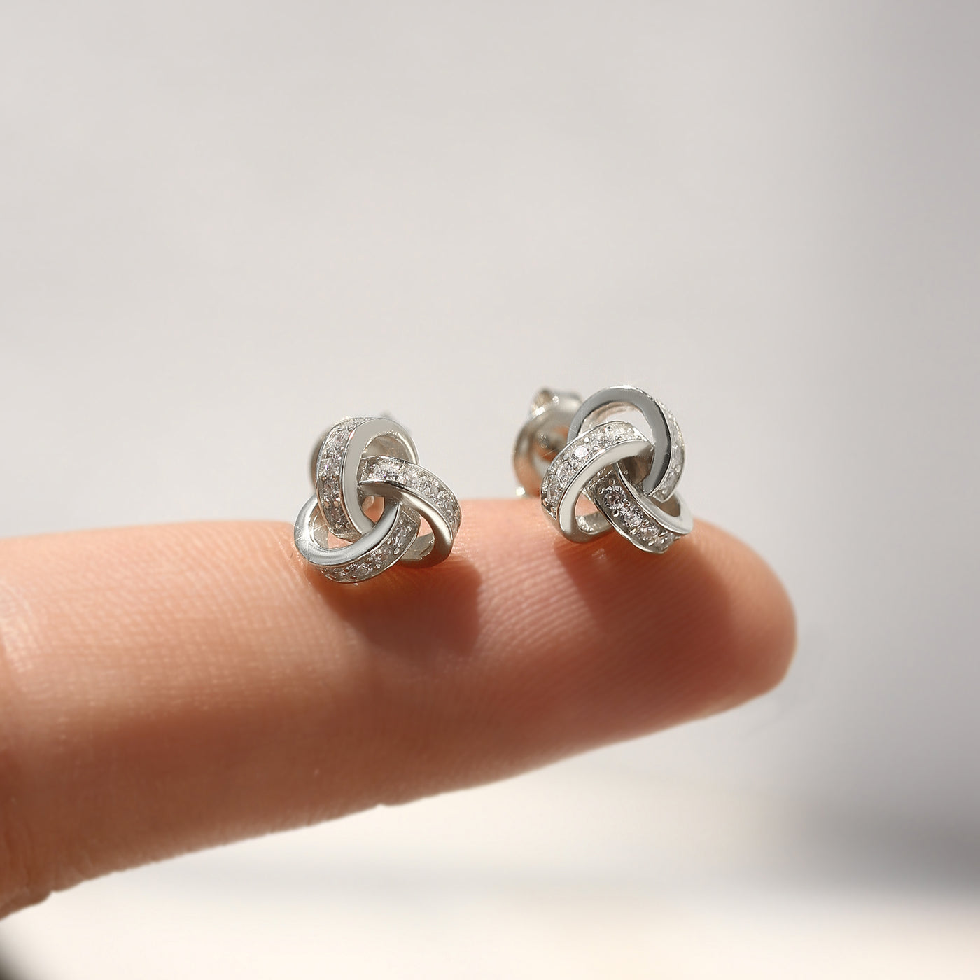 Silver knot earrings on a finger with a blurred background