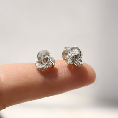 Silver knot earrings on a finger with a blurred background
