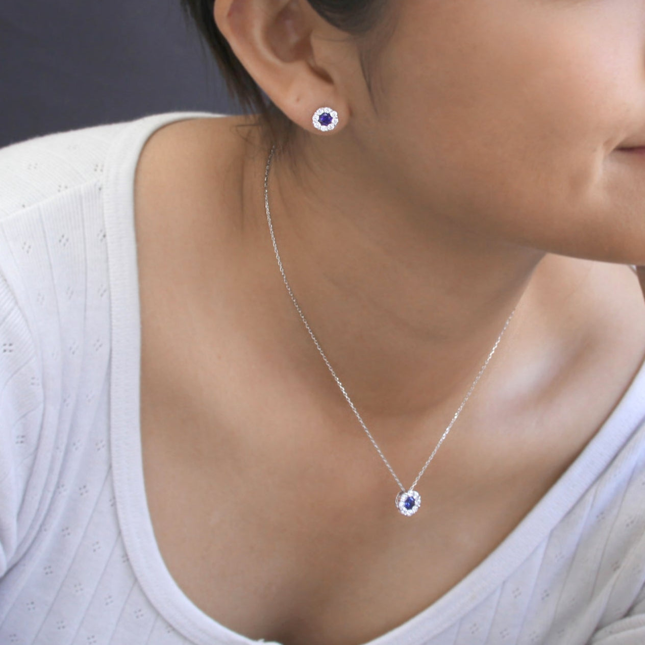 Close-up of a person wearing a silver necklace with a blue gemstone and matching earrings.