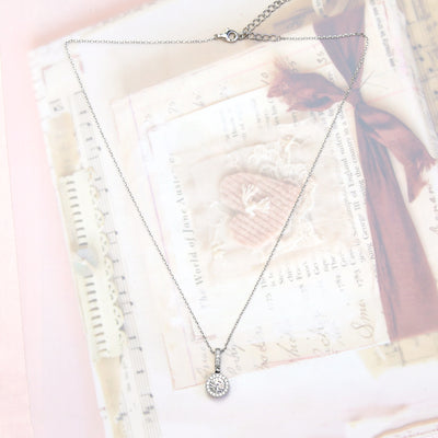 Amore Keeps Necklace with a halo pendant on a textured fabric background