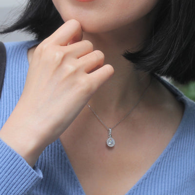 Close-up of a person wearing a silver necklace with a pendant, hand near face.