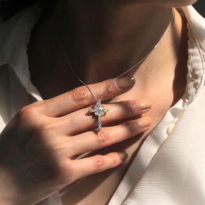 Close-up of a hand holding a silver cross necklace with a pendant.
