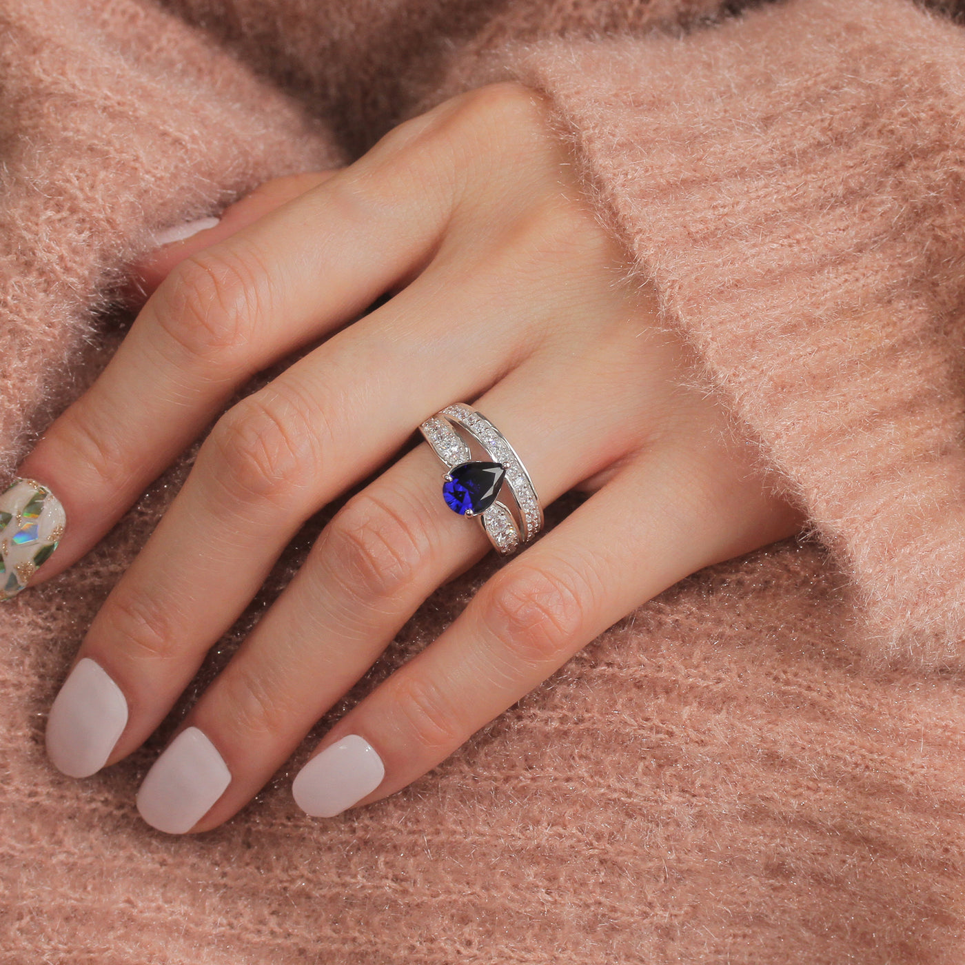 Hand wearing a ring with a blue gemstone on a soft pink background