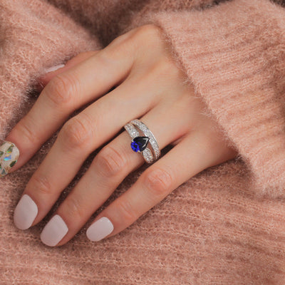 Hand wearing a ring with a blue gemstone on a soft pink background