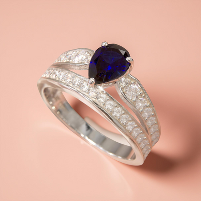 Silver ring with a teardrop-shaped blue gemstone on a pink background