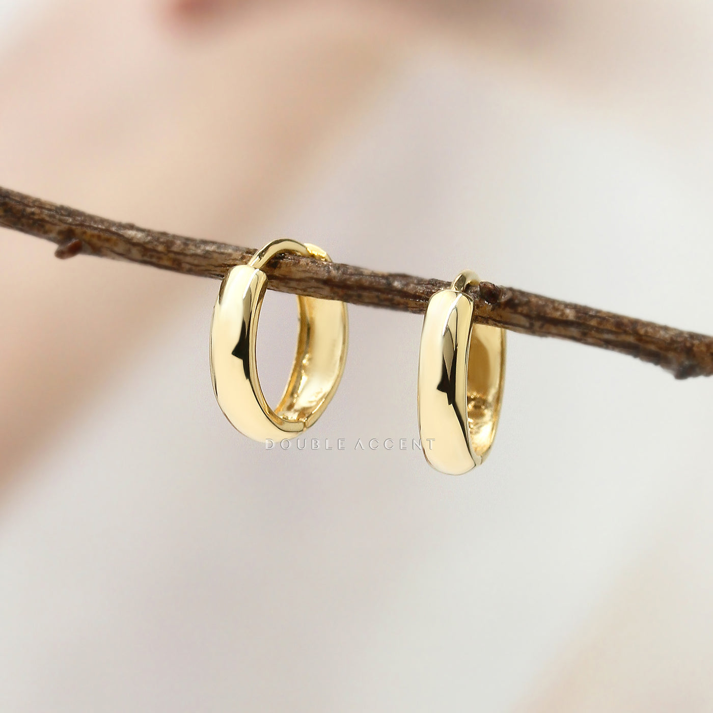 Gold huggie hoop earrings on a branch with a blurred background