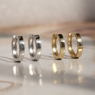 Two pairs of hoop earrings, one silver and one gold, on a reflective surface with 'Double Accent' branding.