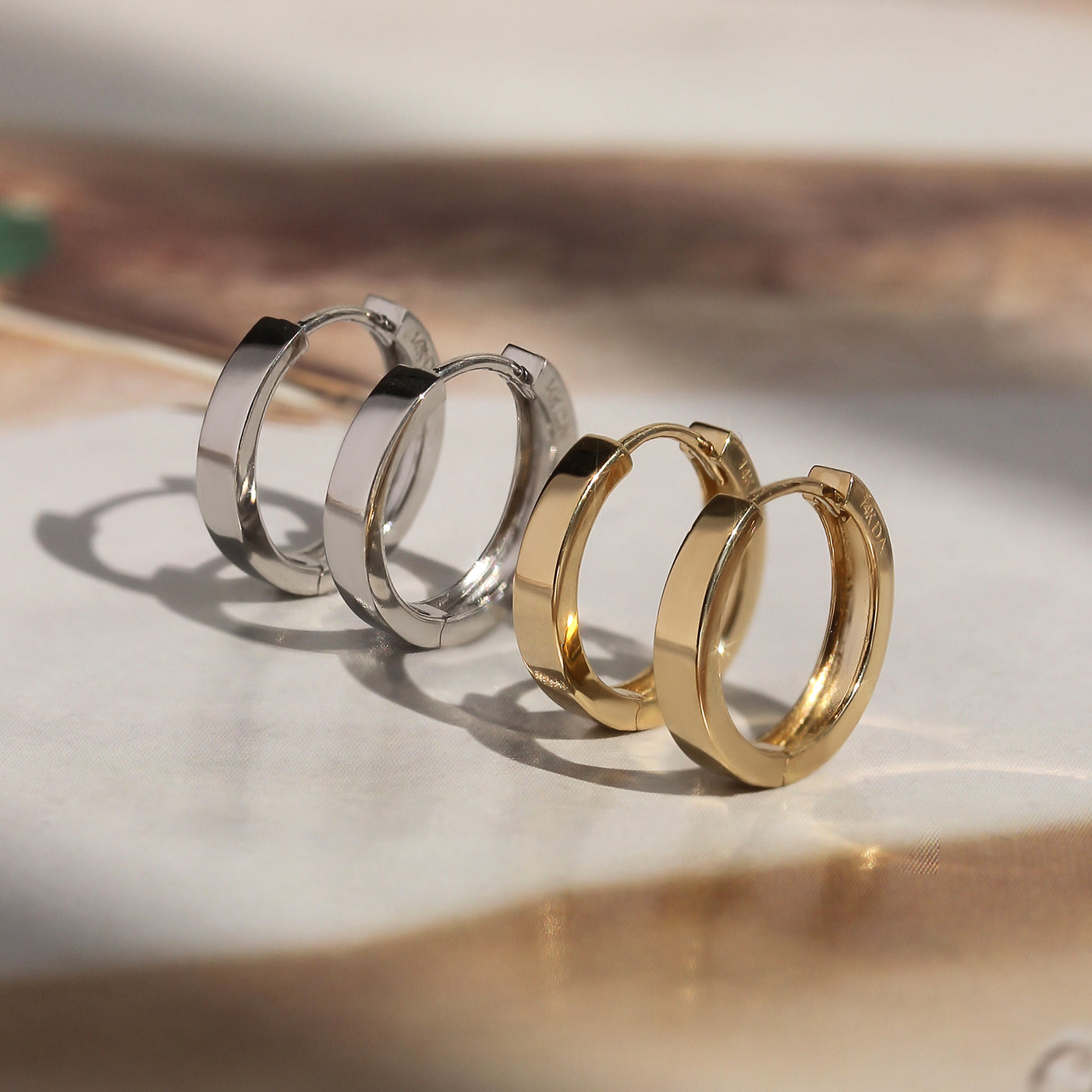 First Shine Huggie Hoops in 14K gold and white gold on soft marble surface