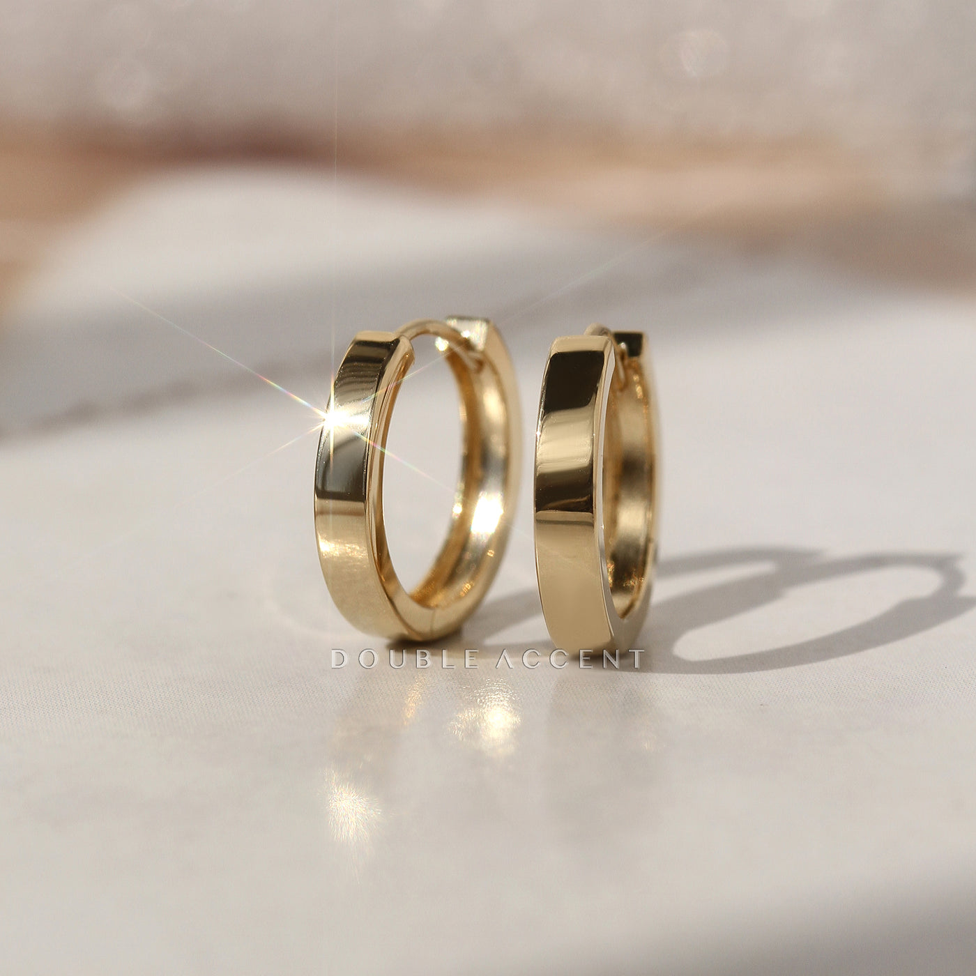 Gold huggies hoop earrings on a reflective surface with a blurred background