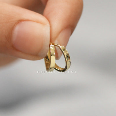 Solid gold hoop earrings held between fingers against a neutral background