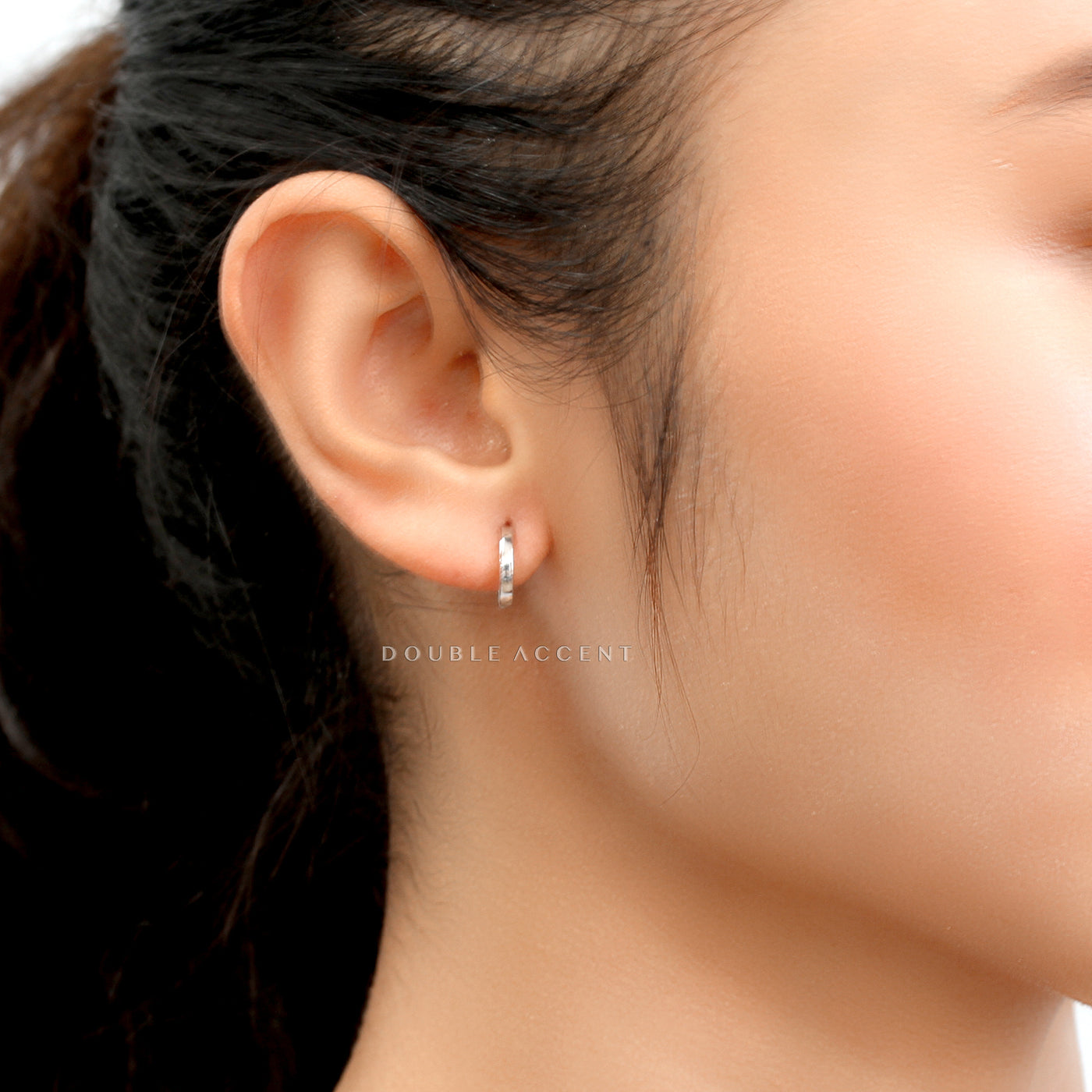 Close-up of an ear wearing a white gold hoop earring with 'DOUBLE ACCENT' branding.