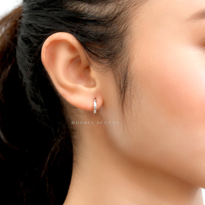 Close-up of an ear wearing a white gold hoop earring with 'DOUBLE ACCENT' branding.