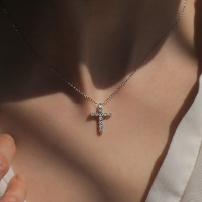 Cross-shaped necklace with diamonds on a person's neck
