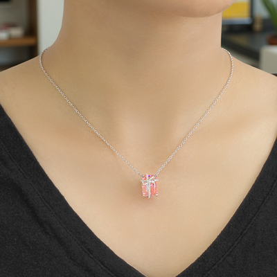 Person wearing a silver necklace with a pink pendant in an indoor setting