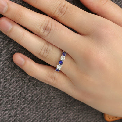 Hand wearing a ring with blue gemstones on a textured gray background
