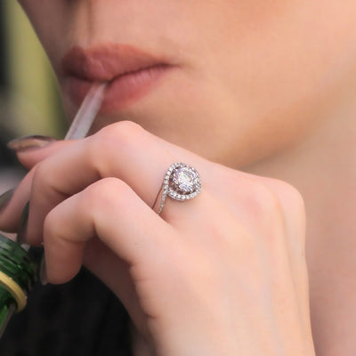 Close-up of a hand with a diamond ring holding a straw, with a blurred background.